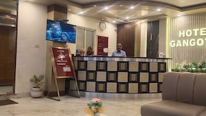 A hotel reception area with a reception desk, a clock, a TV screen, and a sign reading "Hotel Gangotri". - Hotel Gangotri (Haridwar)