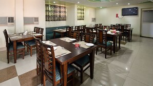 A dining area with multiple tables and chairs, some with placemats and cutlery. - Hotel Gangotri (Haridwar)