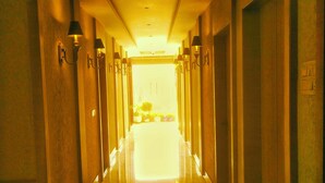 A hotel hallway with a long corridor, wall-mounted lamps, and a reflective floor. - Hotel Gangotri (Haridwar)