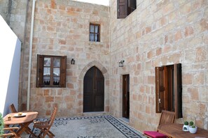 A stone building with a courtyard, featuring a wooden table and chairs, a door, and a small window.