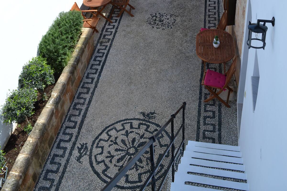Ein Innenhof mit Steinmauern, einem Holztisch und einer Treppe, die zu einer oberen Ebene führt.