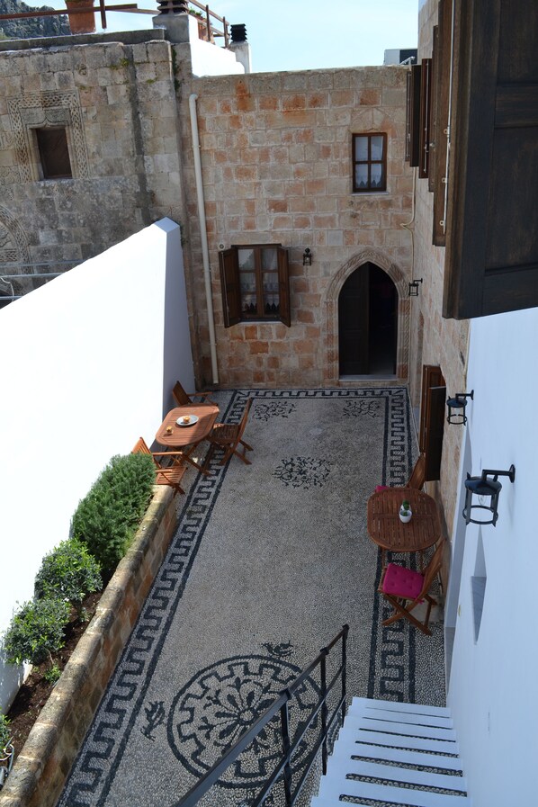 A courtyard with stone walls, a wooden table, and a staircase leading to an upper level.