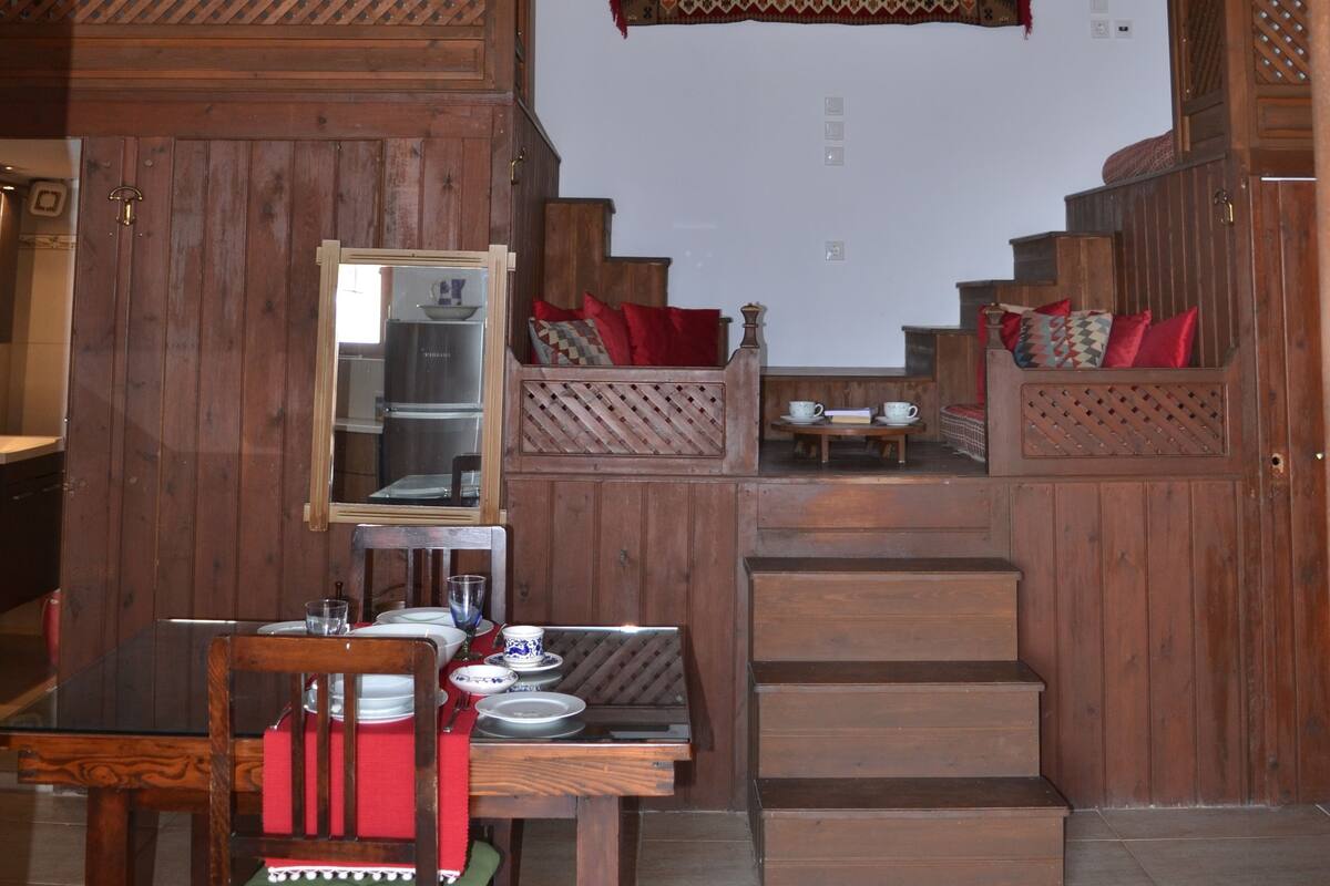Ein Essbereich mit einem Holztisch und Stühlen, einer Kandelaberleuchte sowie einer Treppe zu einer oberen Ebene.