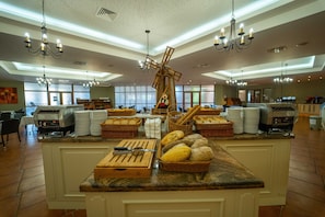 A buffet area with a central wooden windmill decoration, multiple chandeliers, and a variety of breads and pastries on the counter. - HVD Club Hotel Miramar - Ultra All Inclusive (Obzor)