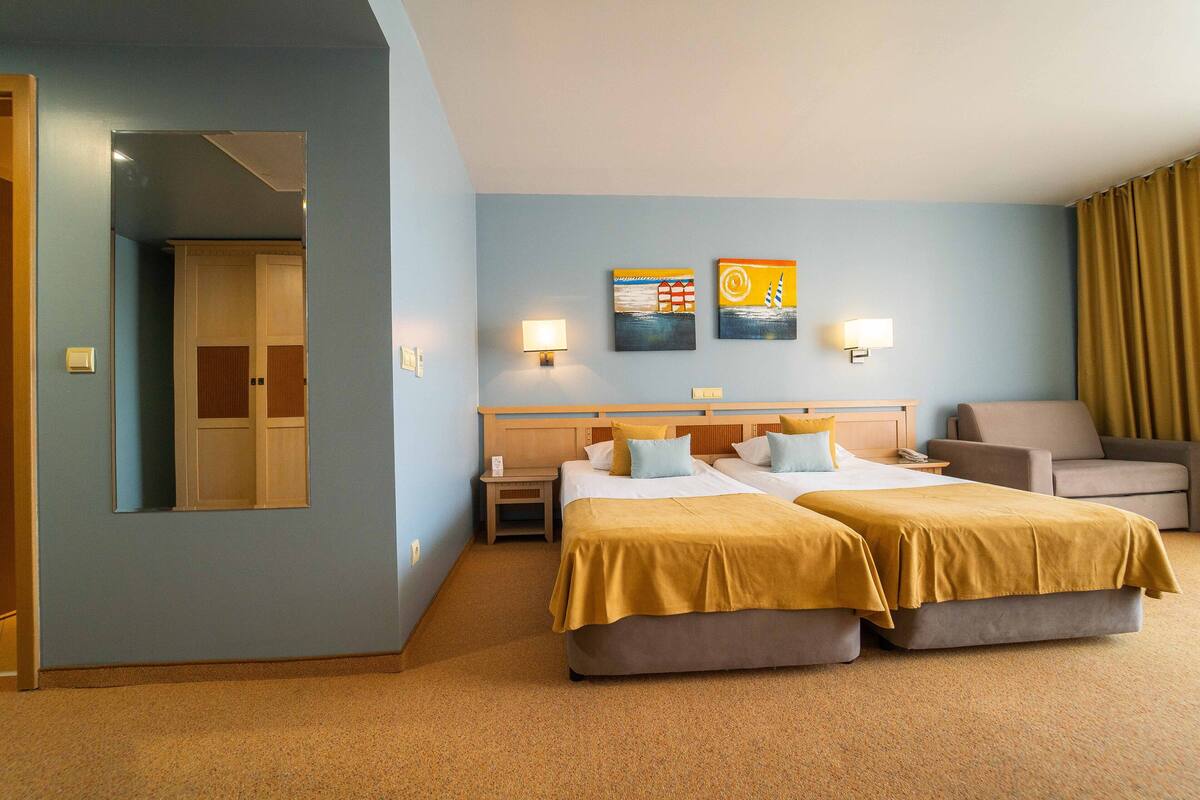 A hotel room with two beds, a sofa, a nightstand, and a mirror.