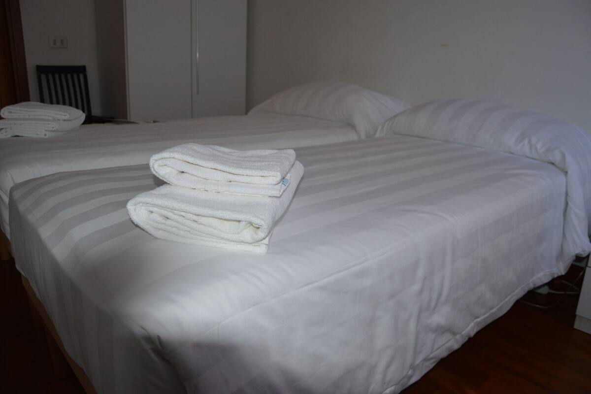 A neatly made bed with white linens and a folded towel on the side.
