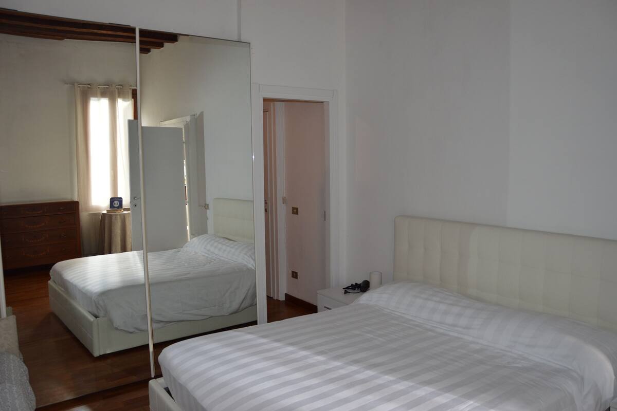 A bedroom with two beds, a mirror, a bedside table, and a wardrobe.