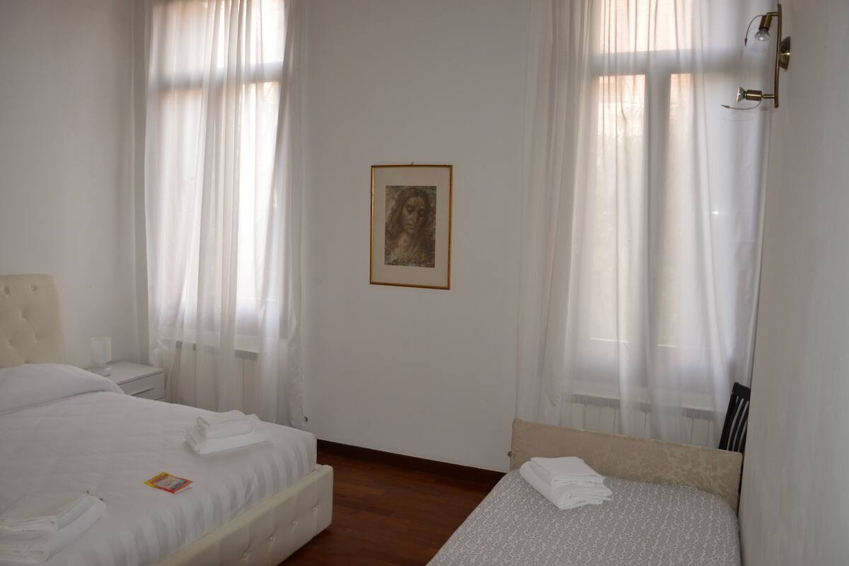 A hotel room with two beds, a framed picture on the wall, and sheer curtains.