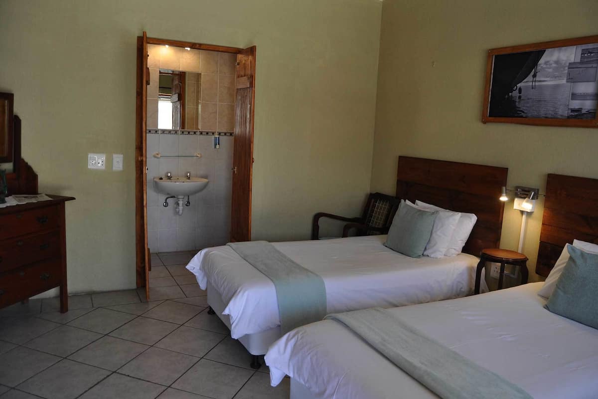 Une chambre d’hôtel avec deux lits, une tête de lit en bois, une petite table, une table de chevet, un miroir et une salle de bain avec un lavabo et un miroir.