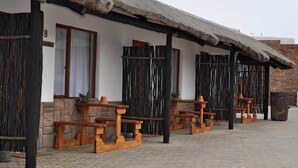 A building with a thatched roof, wooden benches, and a stone wall. - Obelix Guesthouse (Luderitz)