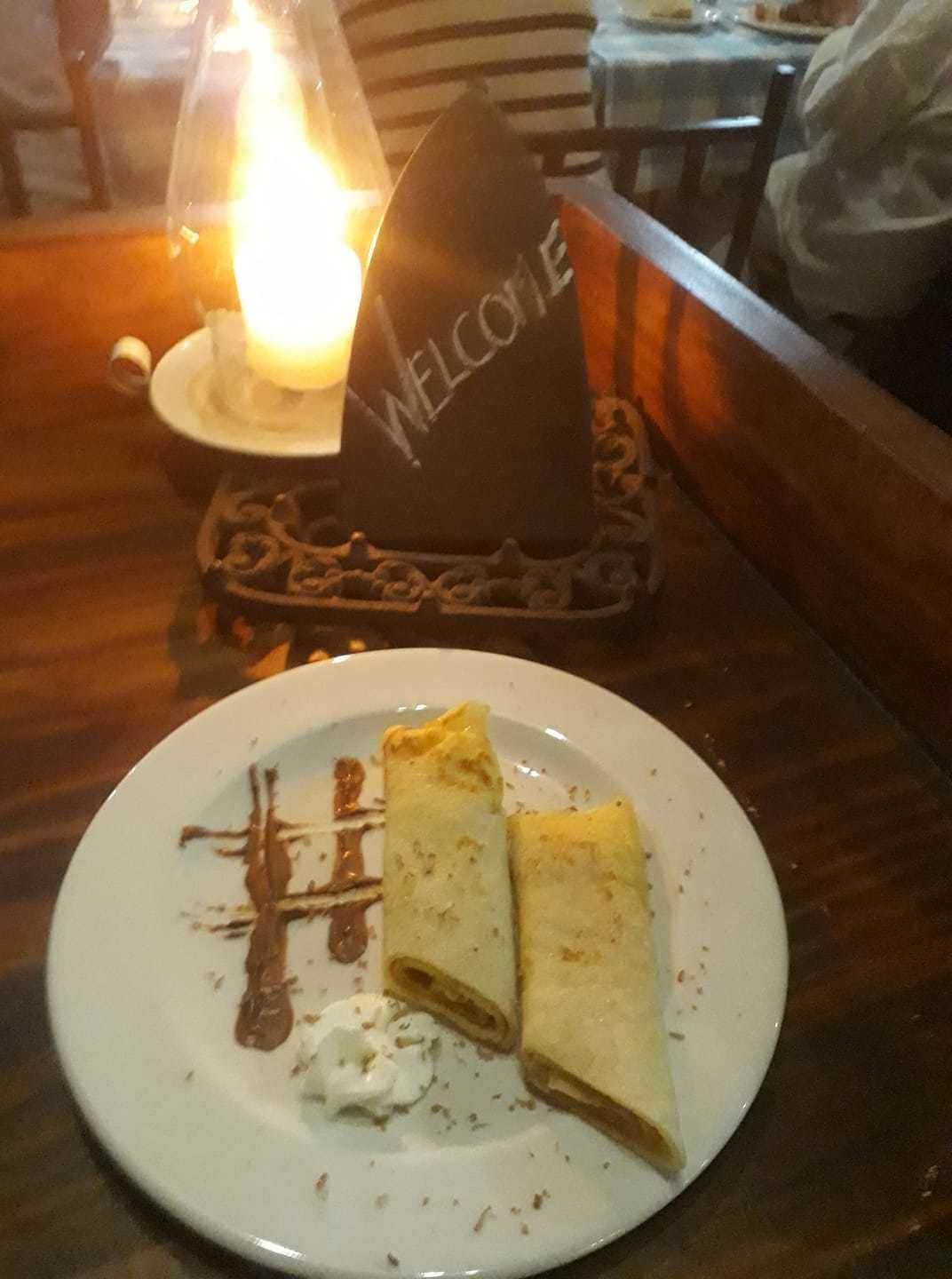 Um prato com uma crepe, chantilly e calda de chocolate, com um letreiro 'WELCOME' ao fundo.
