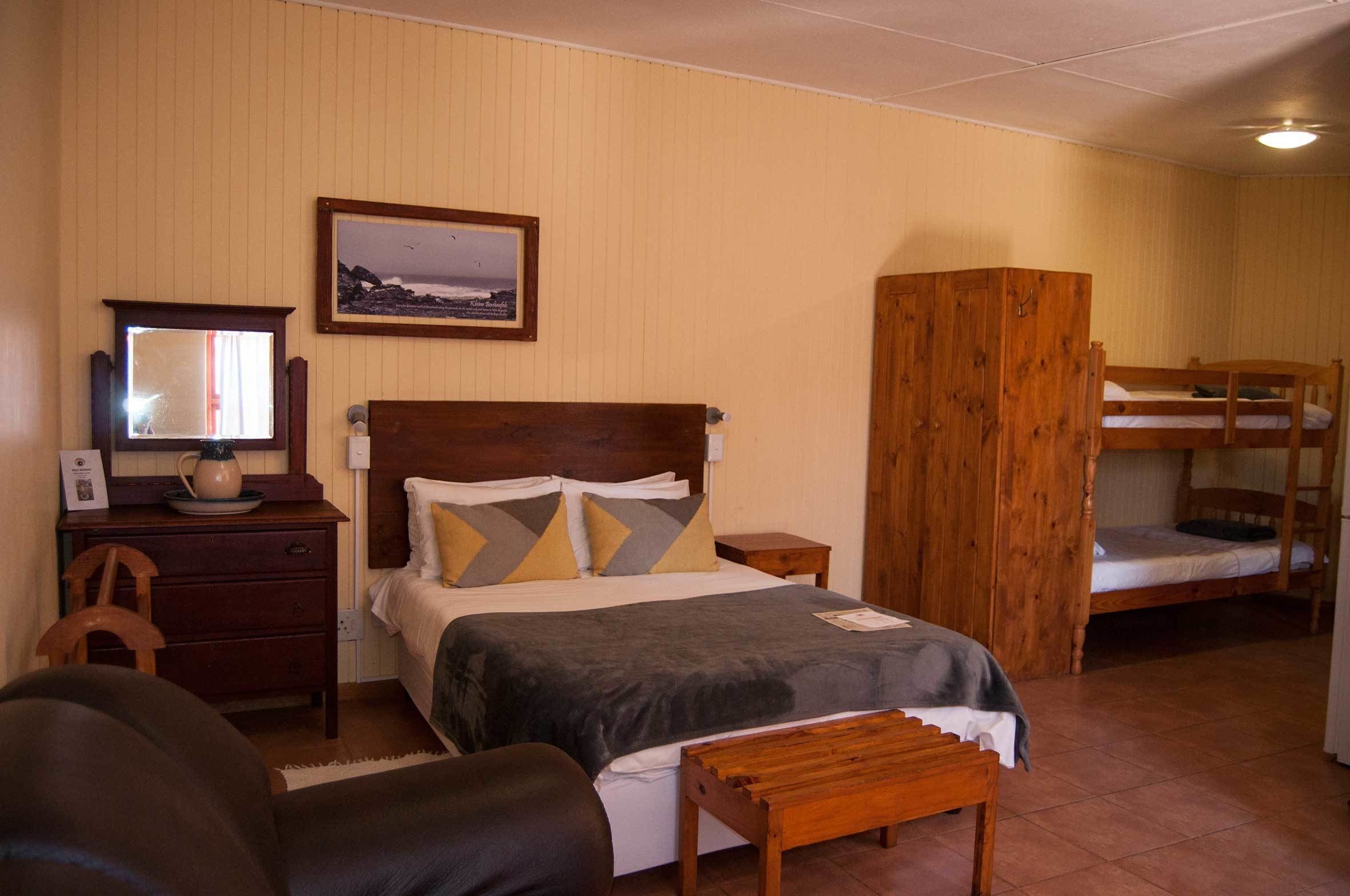 Une chambre avec un lit simple, une armoire en bois, un lit superposé, un bureau avec un miroir et un tableau encadré au mur.