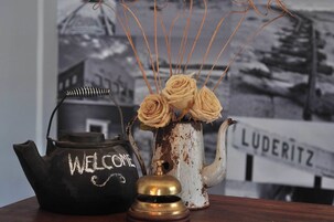 Una tetera negra con la palabra 'WELCOME', un jarrón blanco con rosas y una campana de bronce.