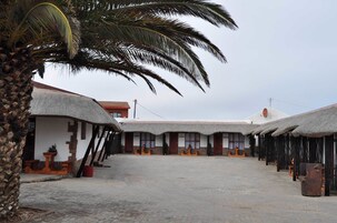 Un patio con edificios de techo de paja, una palmera y suelo empedrado.