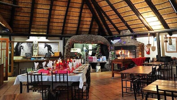 A restaurant with a rustic interior, featuring a stone fireplace, wooden tables, and a thatched roof. - Obelix Guesthouse (Luderitz)