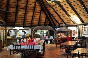 Un restaurante con un interior rústico, que cuenta con una chimenea de piedra, mesas de madera y un techo de paja.