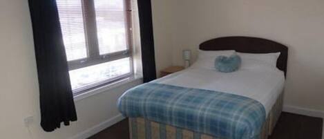 A bedroom with a bed, a window with curtains, and a nightstand.