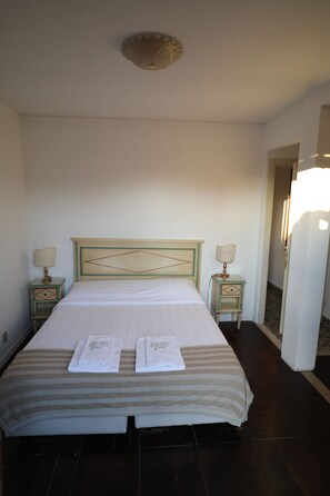 A neatly made bed with two towels, a headboard with a geometric design, two bedside tables with lamps, and a door leading to another room. - Lovely Apartment In Venice (Venice)
