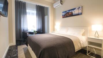 Ett hotellrum med en säng, ett skrivbord, en stol, en tv och en tavla på väggen.