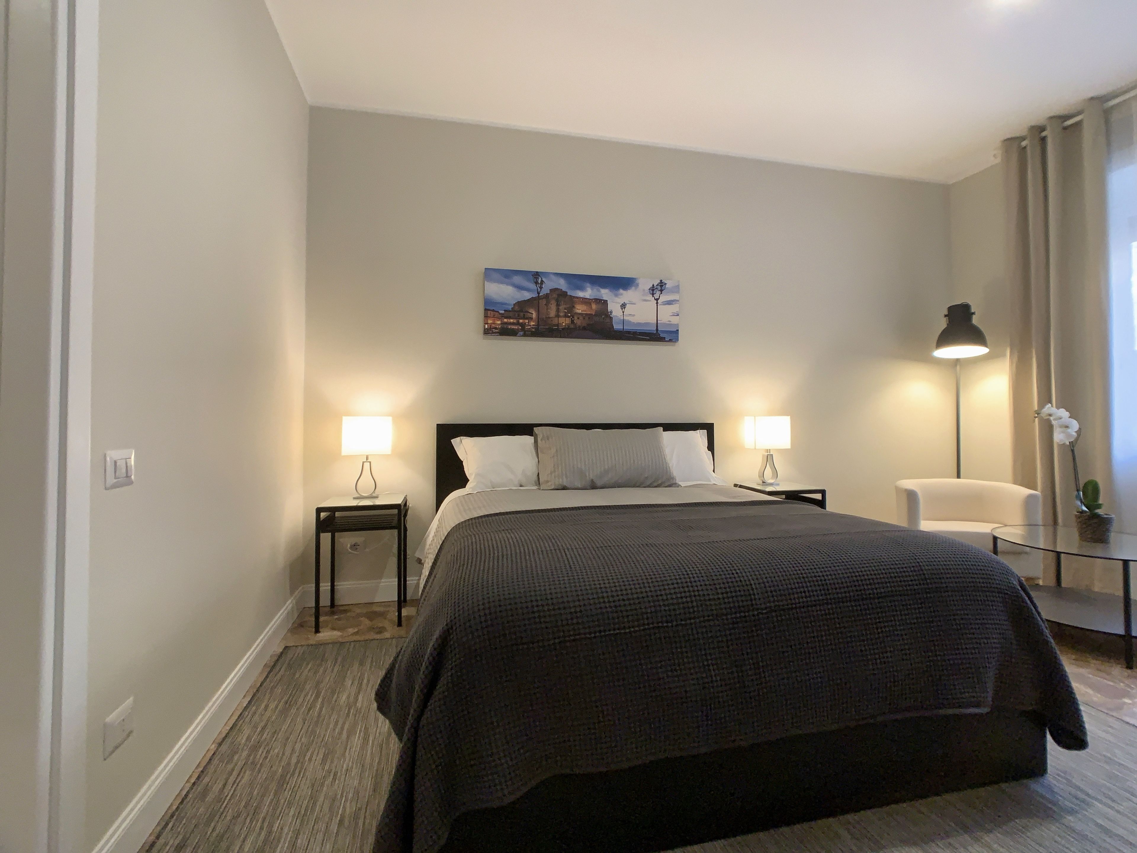 A neatly arranged bedroom with a large bed, two bedside tables with lamps, a chair, and a small table with a plant.