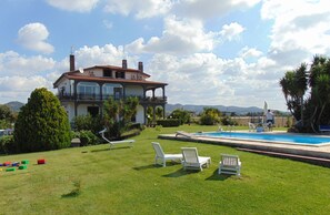 Una casa grande con piscina, rodeada de un césped cuidado y palmeras.