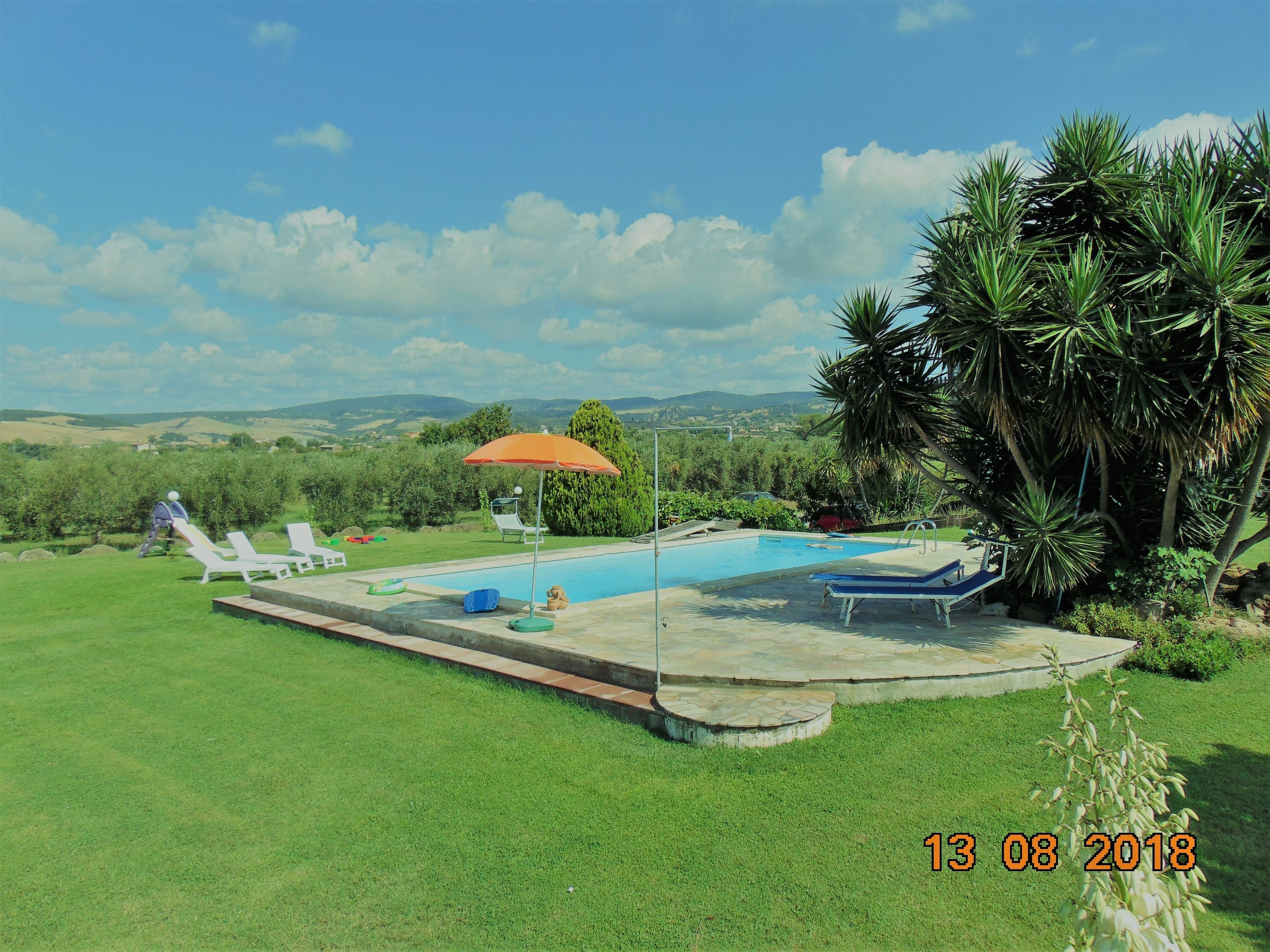 Una piscina con lettini e un ombrellone, circondata dal verde e da dolci colline sullo sfondo.