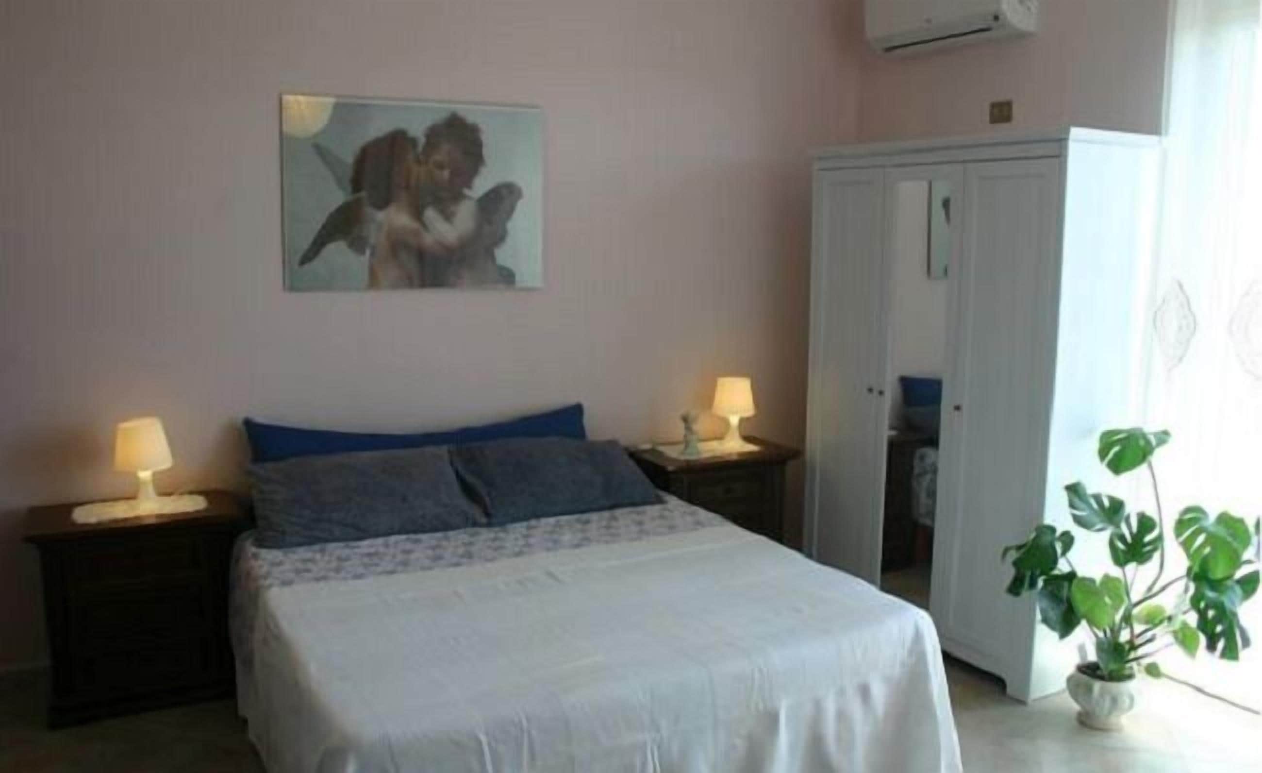 A bedroom with a bed, two bedside tables with lamps, a wardrobe, and a potted plant.