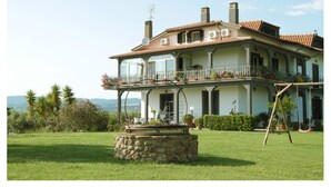 A large, two-story house with a balcony and a stone fountain in the front yard. - B&B La Mia Casa per Tutti (Cerveteri)