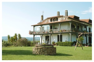 A large, two-story house with a balcony and a stone fountain in the front yard.