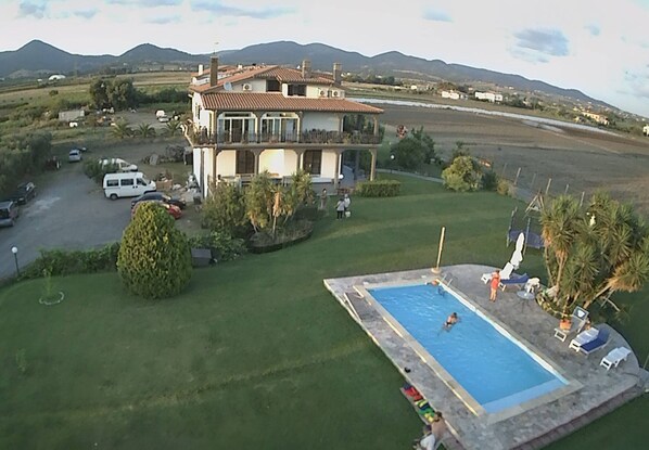 Una casa de dos pisos con piscina, rodeada de césped cuidado y palmeras.