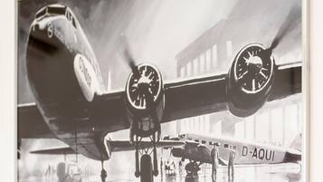 Un vieil avion à hélices, portant l’inscription « D-AQUI » sur le côté, est garé à l’intérieur d’un hangar, avec un bâtiment visible en arrière-plan.