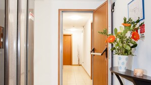 A hallway with a wooden door, a potted plant with orange flowers, and a small table with a candle. - Residence Cigno (Rimini)