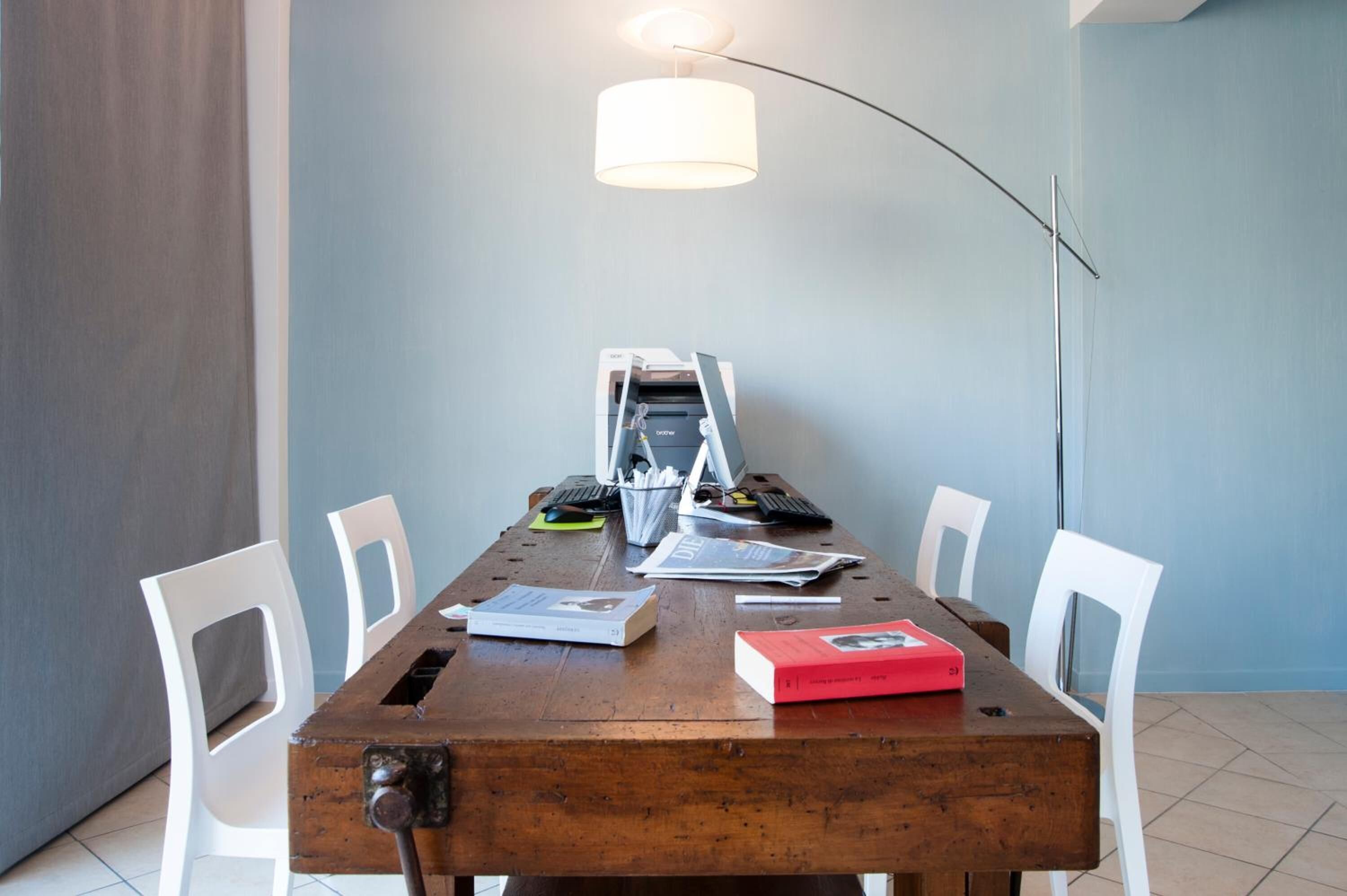 Une salle de conférence avec une table en bois, des chaises blanches, un ordinateur portable, un clavier, une souris et une lampe.