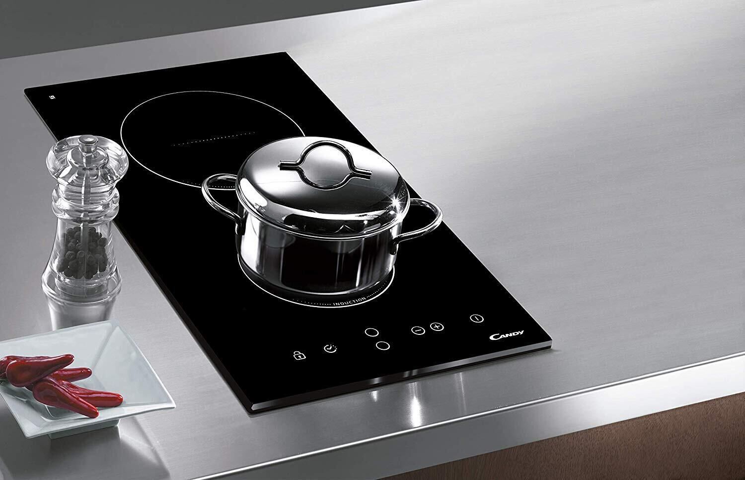 A modern induction cooktop with a pot on it, a salt shaker, and a pair of red scissors on a metallic surface.