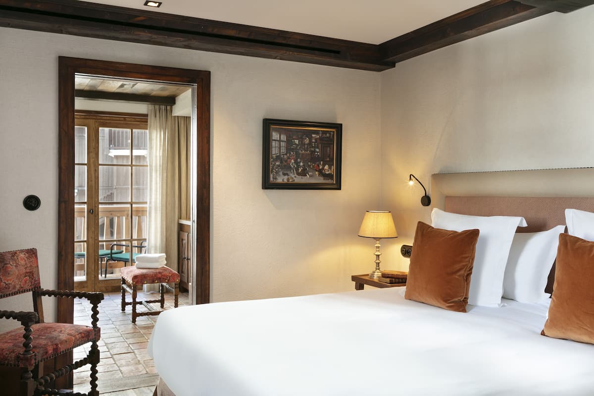 A hotel room with a large bed, a wooden chair, a small table, and a painting on the wall.