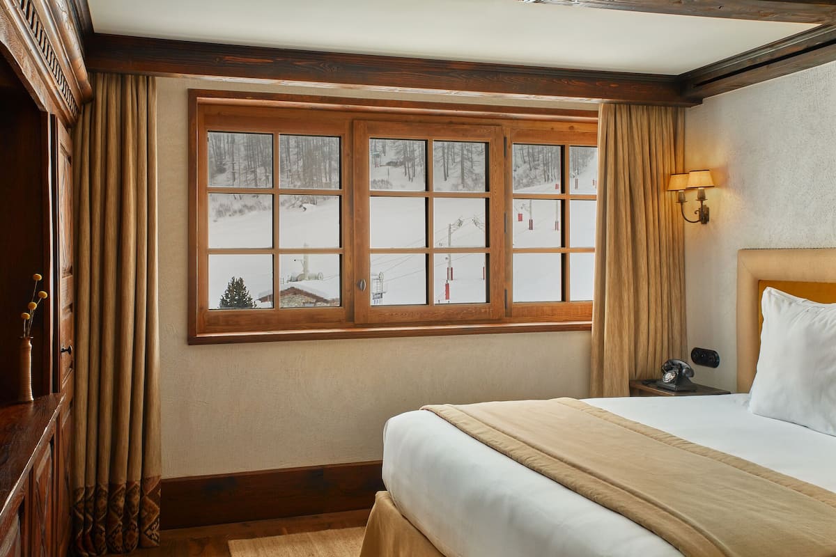 A bedroom with a large window, wooden trim, a bed with white bedding, and a nightstand with a lamp.