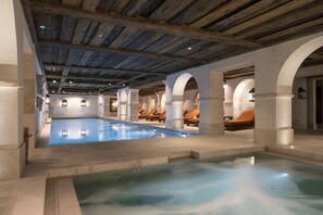A large indoor swimming pool with multiple lounge areas and a rustic wooden ceiling. - Airelles Val d’Isère , Le Brussel's (Val-d'Isere)