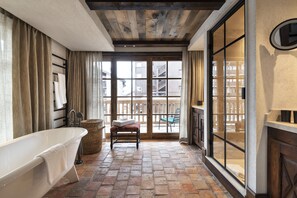 A bathroom with a freestanding bathtub, a bench, and a large window with a view of a balcony.