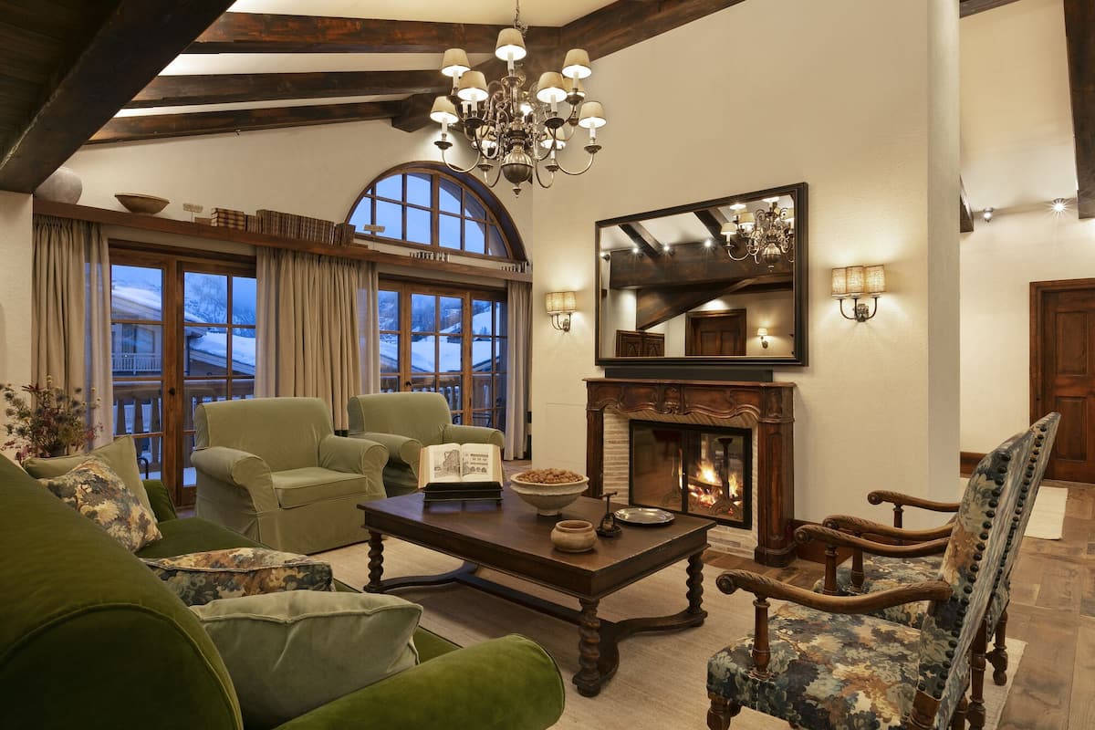 A cozy living room with a fireplace, green sofas, and a large window overlooking a snowy landscape.