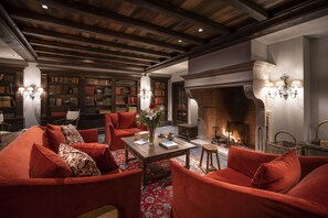 A library with bookshelves, a fireplace, and red upholstered furniture. - Airelles Val d’Isère , Le Brussel's (Val-d'Isere)