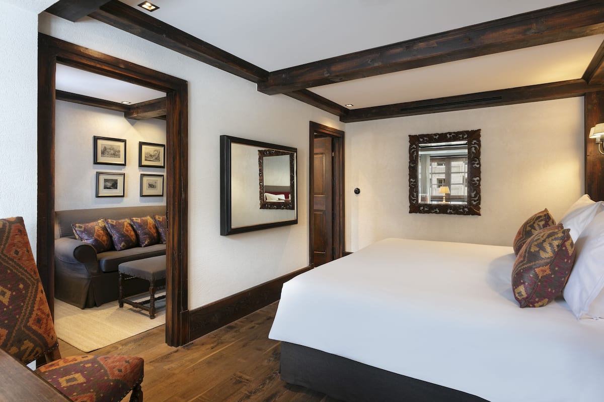 A bedroom with a large bed, wooden beams, a sofa with patterned cushions, and framed pictures on the wall.