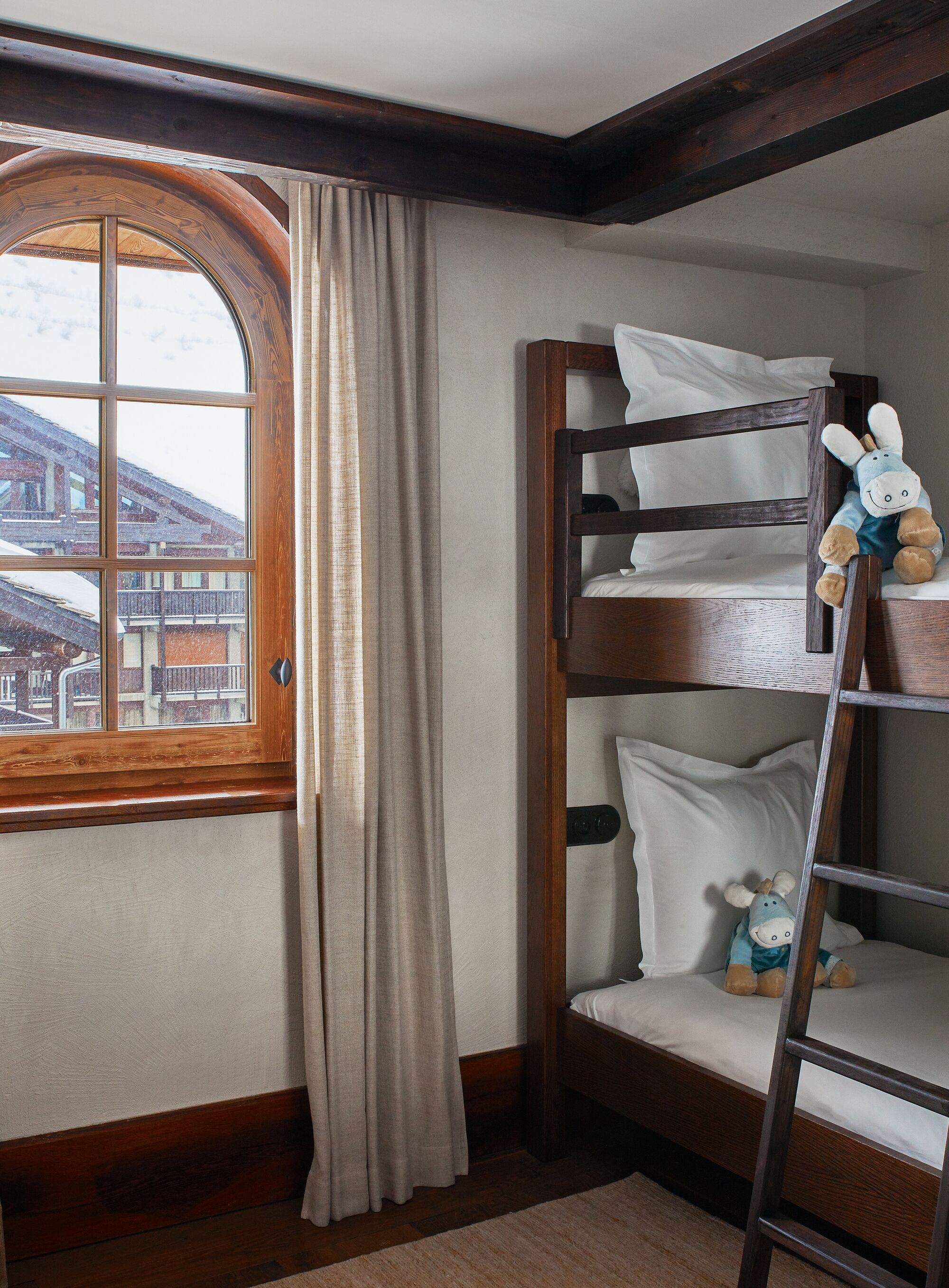 Ein Etagenbett mit einer Leiter, ein Fenster mit Vorhängen und ein Blick auf Gebäude im Freien.