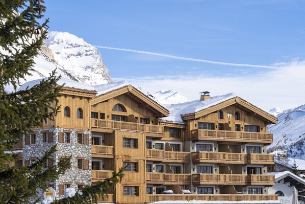A multi-story wooden building with balconies, surrounded by snow-covered mountains. - Airelles Val d’Isère , Le Brussel's (Val-d'Isere)