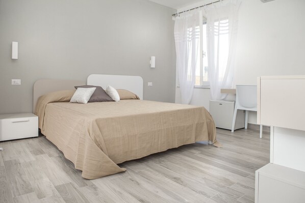 Un dormitorio minimalista con cama, mesitas de noche, escritorio y silla.