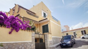 A two-story building with a stone base and a yellow facade, a black gate, and a parked car.