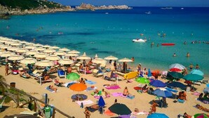 A beach with numerous umbrellas and people sunbathing.