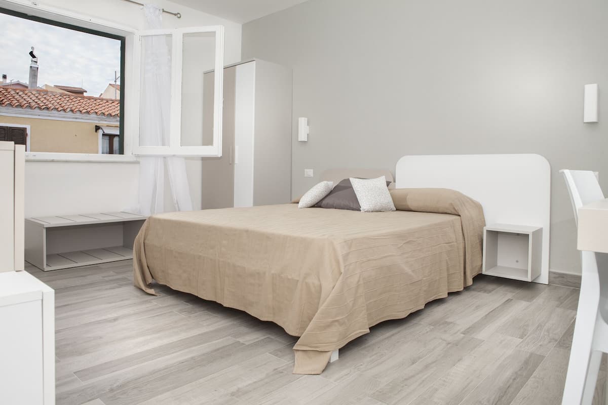 Un dormitorio moderno con cama, ventana y vista a edificios.