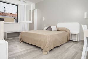 Un dormitorio moderno con cama, ventana y vista a edificios.
