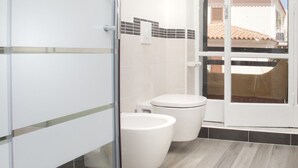 A modern bathroom with a glass shower enclosure, a toilet, and a bidet.