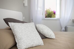 Ein Bett mit zwei Kissen, ein Fenster mit Vorhängen und eine Blumenansicht nach draußen.